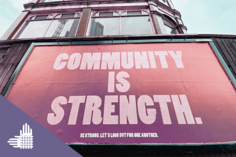 A photo of a billboard is shown with an orange and purple filter. It contains large white text reading, "COMMUNITY IS STRENGTH" Underneath is smaller white text: "BE STRONG. LET'S LOOK OUT FOR ONE ANOTHER." An element of the Partnership's logo, intertwined hands in white, is shown against a purple rectangle in the lower left-hand corner.