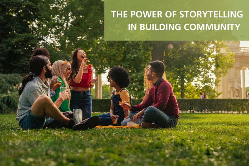 In the background is an image of a diverse group of people sitting in a circle and laughing while eating. In the upper right-hand corner is a semi-translucent green rectangle containing white text. It reads, "THE POWER OF STORYTELLING IN BUILDING COMMUNITY".