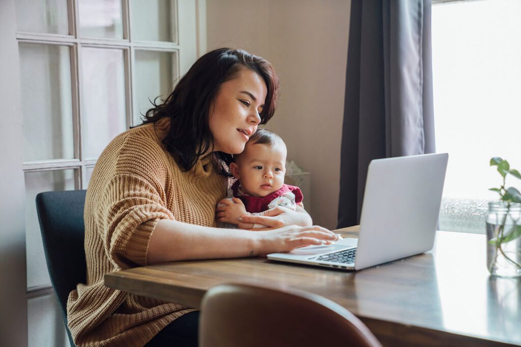 Mom holding her baby while on the laptop